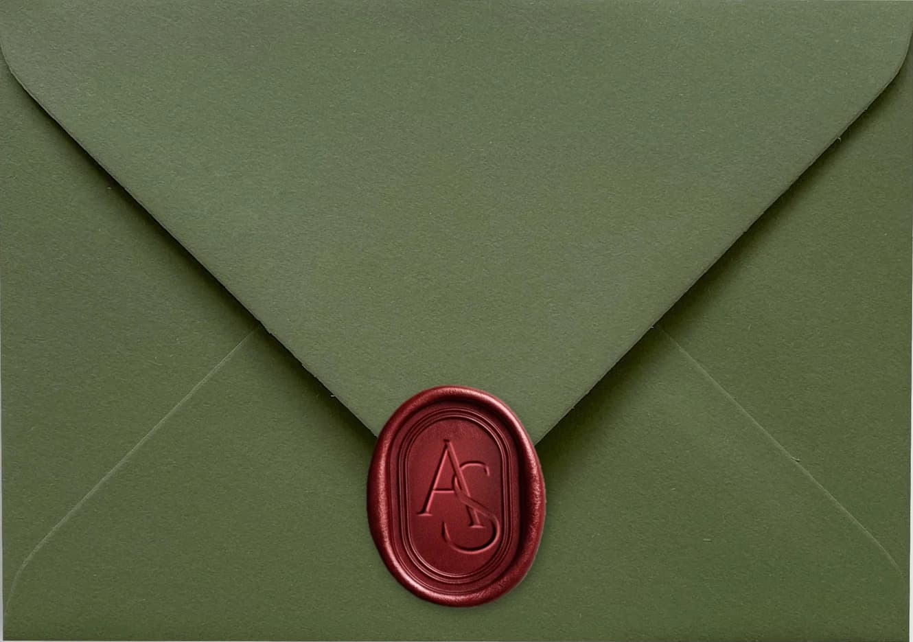 A sage green envelope sealed with a burgundy wax monogram
